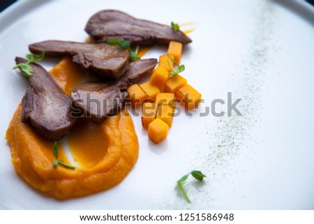 beef tongue cut into pieces with pieces of orange pumpkin lies on a white plate 