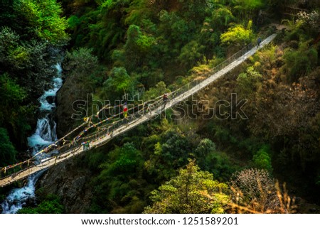 Sherpa with baggage crossing sunlit suspension bridge in Nepal, Langtang valley