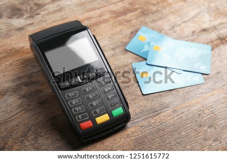 Modern payment terminal and credit cards on wooden background