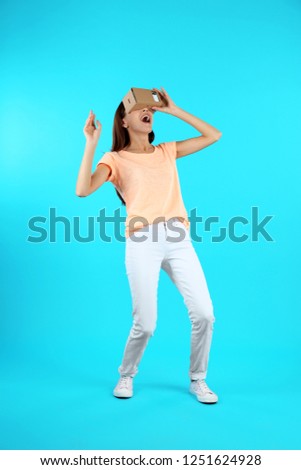 Young woman using cardboard virtual reality headset on color background
