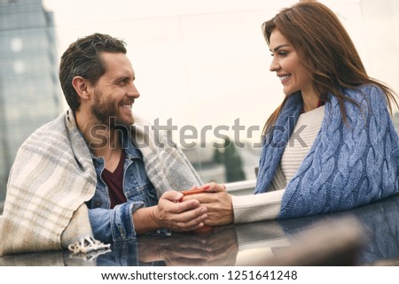 Waist up portrait of smiling male and female is spending time in beautiful terraca while holding cup together