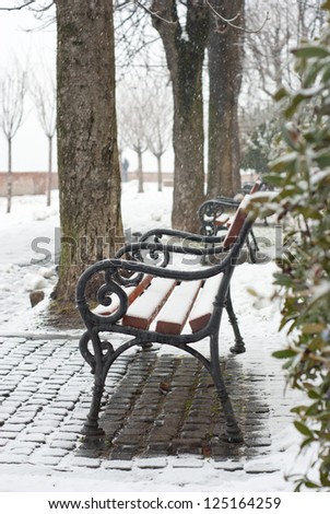 park bench on a winter alley at snowfall