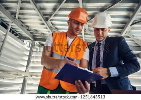 Waist up photo of young construction engineer is showing construction plan to his project manager