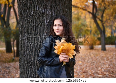 Pretty woman posing with maple's leaves in autumn park near big tree. Beautiful landscape at fall season.
