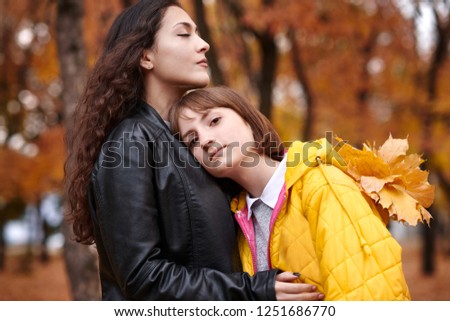 Pretty woman and teen girl are posing with bunch of maple's leaves in autumn park. Beautiful landscape at fall season.