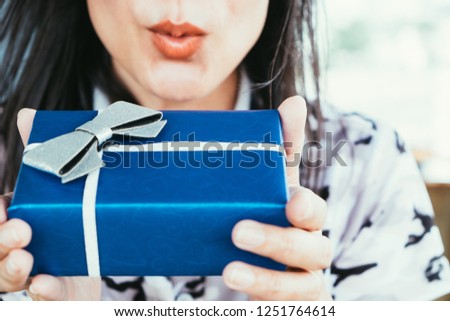 Closeup lips of excited cute girl holding blue gift box wrapped in ribbon bow. Young woman receiving present package. Merry Christmas, Happy new year, Anniversary Birthday, Valentine's day. Copy space
