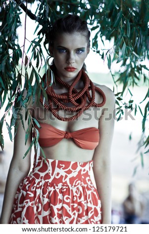 Young model on the beach near a tree with bright make-up in a skirt and a scarf creative