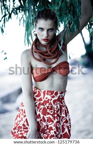 Young model on the beach near a tree with bright make-up in a skirt and a scarf creative