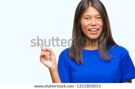 Young asian woman over isolated background with a big smile on face, pointing with hand and finger to the side looking at the camera.