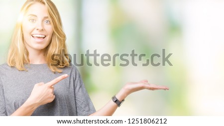 Beautiful young woman wearing oversize casual t-shirt over isolated background amazed and smiling to the camera while presenting with hand and pointing with finger.