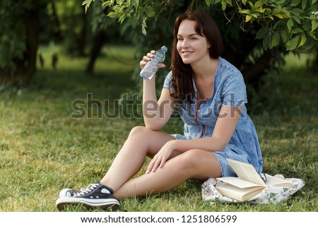 Young pregnant girl drinking bottled water in the park.