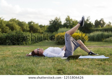Beautiful big girl lying on the green grass in park with her laptop and relaxing.