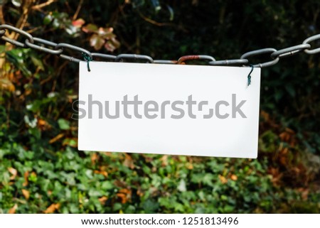 White sign hanging on a chain on forest background, copy space, text place