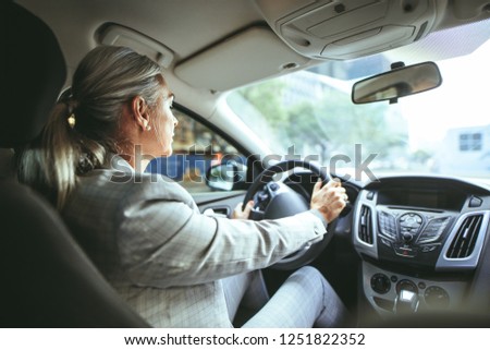 Businesswoman driving a car. Shot from behind of senior female in businesswear driving a car. Royalty-Free Stock Photo #1251822352