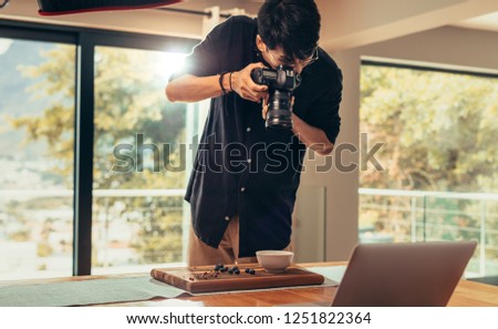 Professional food photographer making shot of food for advert. Male photographer taking pictures of food on wooden board on table with professional camera.