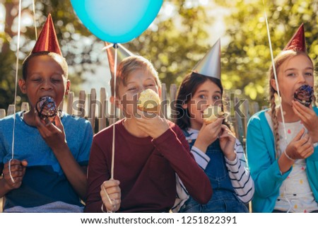 Group of kids wearing party hats holding balloons and enjoying eating cupcakes at a party. Little girls and boys having a party together.