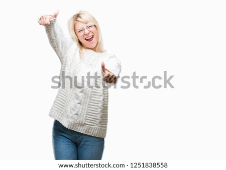 Young beautiful blonde woman wearing winter sweater and glasses over isolated background approving doing positive gesture with hand, thumbs up smiling and happy for success. Looking at the camera
