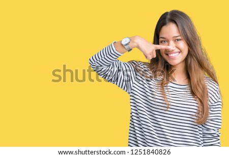 Young beautiful brunette woman wearing stripes sweater over isolated background Pointing with hand finger to face and nose, smiling cheerful