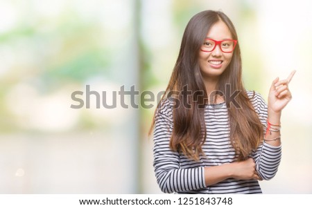 Young asian woman wearing glasses over isolated background with a big smile on face, pointing with hand and finger to the side looking at the camera.