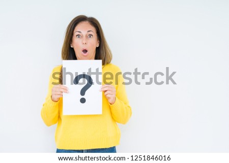 Middle age woman thinking and holding paper with question mark symbol over isolated background scared in shock with a surprise face, afraid and excited with fear expression