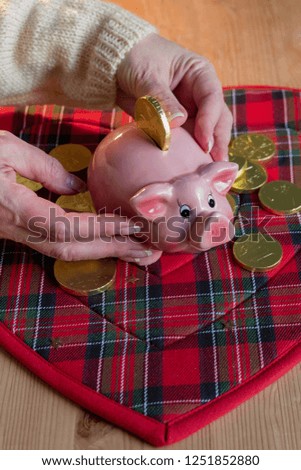 Female hands holds Piggy bank for luck on the background of chocolate coins and wooden table with the serving napkin.Low angel view.