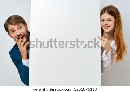 Funny man and woman peeking out from behind a white mockup                    
