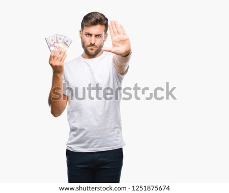 Young handsome man holding stack of dollars over isolated background with open hand doing stop sign with serious and confident expression, defense gesture