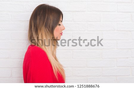 Young adult woman over white brick wall wearing winter outfit at home looking to side, relax profile pose with natural face with confident smile.