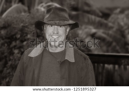 Portrait of senior man smiling outdoors in the rain wearing a cowboy hat and coat