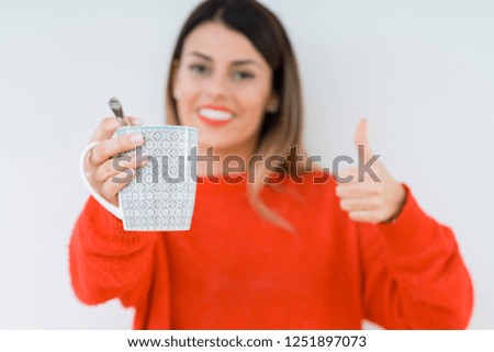 Young woman drinking cup of coffee over isolated background happy with big smile doing ok sign, thumb up with fingers, excellent sign