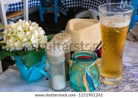 Picture of cafe table with glass of beer, flowers and hat