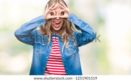Beautiful young blonde woman over isolated background doing ok gesture like binoculars sticking tongue out, eyes looking through fingers. Crazy expression.