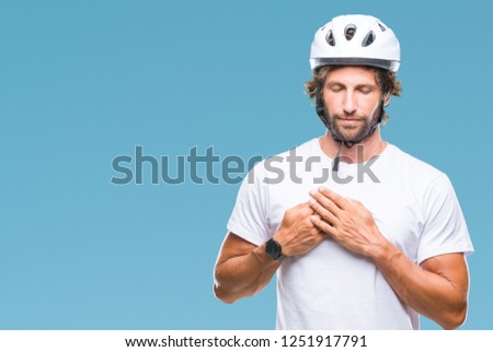 Handsome hispanic cyclist man wearing safety helmet over isolated background smiling with hands on chest with closed eyes and grateful gesture on face. Health concept.
