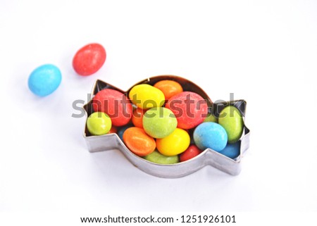A cookie cutter in the shape of a candy lies on a white background and is filled with colorful chocolate lentils - Concept with sweet colorful chocolate lentils in Christmas shapes with space for text