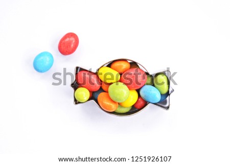 A cookie cutter in the shape of a candy lies on a white background and is filled with colorful chocolate lentils - Concept with sweet colorful chocolate lentils in Christmas shapes with space for text