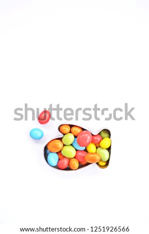 A cookie cutter in the shape of a glove lies on a white background and is filled with colorful chocolate lentils - Concept with sweet colorful chocolate lentils in Christmas shapes with space for text