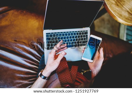 Man sharing media files via laptop and smartphone devices using bluetooth connection indoors, cropped image of male hands using application on modern technology for communication with colleagues