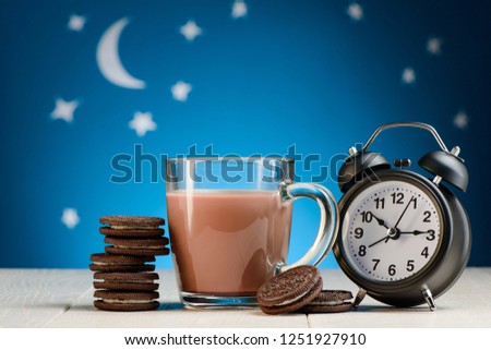 Sweet cookies, cocoa and clock on bedside table under blue starry sky. Cute concept of bedtime food and drinks.