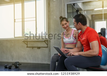 Women are discussing fitness with trainers. Young female talking during workout in gym. Female coach explaining directives with laptop or computer.