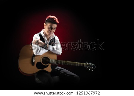 Woman musician with red hair in a black suit and white shirt with a guitar on a black background