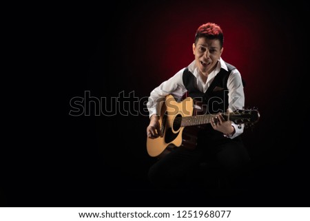 Woman musician with red hair in a black suit and white shirt with a guitar on a black background