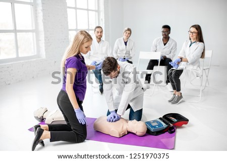 Group of young medics practising to make artificial breathing with medical dummies during the first aid training in the white room Royalty-Free Stock Photo #1251970375