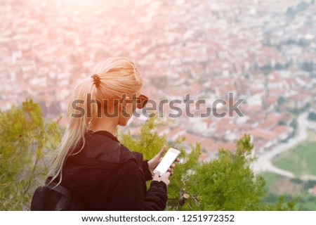 Teenage blonde girl using smartphone in mountains, mobile with blank mockup.
