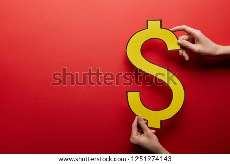 elevated view of hands holding yellow dollar sign on red background