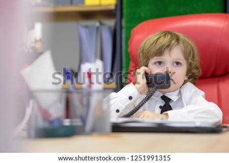 Little boy sits in the office in the chair and talking on the phone. Little boss.