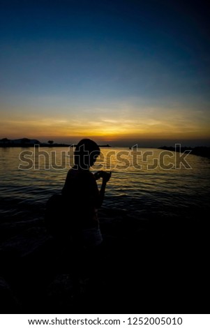 silhouette of a woman holding a smartphone at sea side during sunrise or sunset.