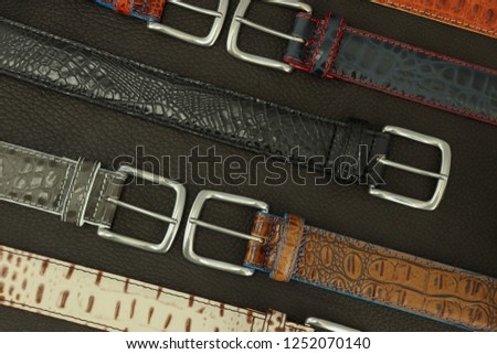Genuine crocodile leather belts for men, laying on a dark leather background.