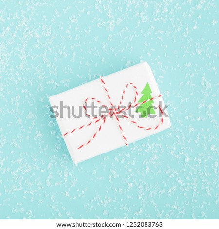 Modern Christmas present wrapped in white paper and red string on a blue snowflake background - flat lay.