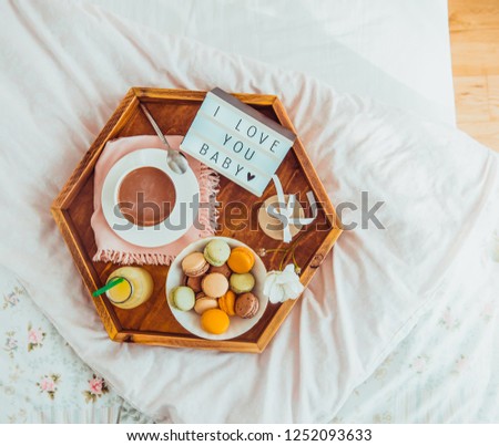 Romantic Breakfast in bed with I love you baby text on lighted box. Cup of coffee, juice, macaroons, flower and gift box on wooden tray. Birthday, Valentine's day morning. Top view. Copy space