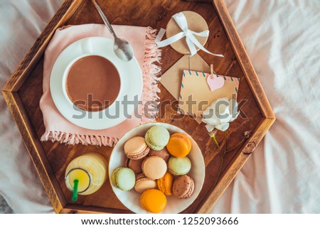 Breakfast in bed with empty blank card for text. Cup of coffee, juice, macaroons, rose flower and giftbox on wooden tray. Romantic breakfast in bed. Birthday, Valentine's day morning. Copy space